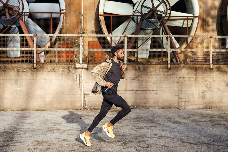 MNSTRY Athlet Amanal Petros rennt mit MNSTRY Trinkflasche durch ein Industriegebiet